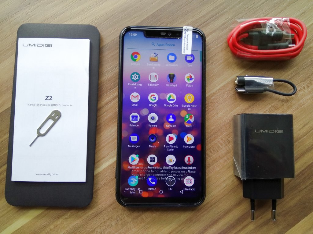 Lieferumfang: Kurzanleitung, SIM-Schacht-Stecker, Gerät mit Schutzcover (hier montiert), Displayschutzfolie, USB-Kabel, EU-Schnellladenetzteil und USB-Kopfhöreradapter.